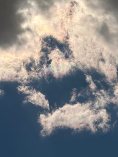 The image captures a sky with clouds displaying iridescence. The cloud formations are predominantly white and gray, with some areas exhibiting a rainbow-like sheen due to diffraction. The background is a deep blue, representing a clear sky. The scene is suggestive of a natural, outdoor setting. The location of Apnagyugh, Armenia, is inferred from the image’s metadata.