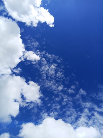 The image depicts a vibrant blue sky filled with scattered white clouds. The clouds vary in size and density, with some appearing as large, fluffy masses along the left and bottom edges of the frame, and others as smaller, wispy formations spread across the sky. A subtle ray of light is visible in the upper right corner, suggesting a sunny day. There are no people, objects, or structures visible in the image, only the natural elements of sky and clouds. The scene is devoid of any urban context, making it impossible to ascertain its location within Raygorodok, Kazakhstan.