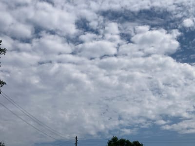 This media file depicts a cloudy sky over a rural scene in Rakity, Russia. The sky is filled with a variety of cumulus and stratus clouds, with patches of blue sky visible in between. The clouds are predominantly white and gray, suggesting a partly cloudy or overcast day.
In the foreground, several power lines stretch horizontally across the frame, supported by utility poles. Some foliage, likely trees, is visible on the left and right edges of the image, indicating a natural environment. The overall impression is of a typical day in a rural or suburban setting, characterized by cloud cover and infrastructure elements.
The time of day appears to be daytime, given the brightness of the sky and the presence of shadows, though the exact time is difficult to determine due to the cloud cover. The weather is clearly cloudy. There is no visible text in the image.