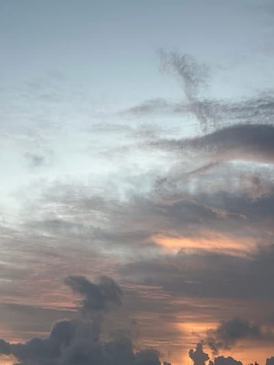 This image captures a dramatic sunset sky over Midigama, Sri Lanka. The clouds are the primary subject, displaying a range of textures and colors. On the left side of the frame, the sky is a soft, pale blue, gradually transitioning into more textured, wispy clouds. As the eye moves to the right, the clouds become more defined and dramatic.

The right side of the image is dominated by thick, dark gray clouds, interspersed with streaks of golden and orange light. These vibrant colors suggest the sun is low on the horizon, painting the sky with warm hues. The light filters through the clouds, creating a sense of depth and movement. Some of the clouds are sharply defined, appearing almost like abstract sculptures against the illuminated sky.

The overall impression is one of a powerful and dynamic natural spectacle. The contrast between the dark clouds and the bright sunlight creates a sense of awe and wonder. There are no people or objects visible, focusing the viewer's attention entirely on the celestial display. The time of day is clearly sunset, and the weather is characterized by cloudy conditions that are being dramatically illuminated. The location cue is Midigama, Sri Lanka, suggesting a coastal or tropical setting where such vibrant sunsets are common. There is no visible text in the image.