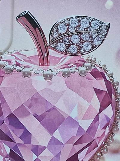 This is a close-up, angled shot of a faceted pink crystal apple, adorned with pearls around its circumference and a leaf made of small diamonds attached to its stem. The background is a soft, out-of-focus pink. There is no discernible location in the city of Fresnes, France, nor are there any people or actions depicted.