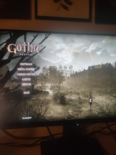 The image shows the main menu of the video game "Gothic Remake." The menu options are displayed in Spanish: "Continuar" (Continue), "Nueva Partida" (New Game), "Cargar Partida" (Load Game), "Ajustes" (Settings), "Créditos" (Credits), and "Salir" (Exit). The game's title "Gothic Remake" is prominently displayed at the top left. The background is a rendered scene of a dark, misty forest with a path leading towards a fortified settlement. There is no indication of the image's location in the city of Figueres, Spain; this is a scene from a video game.