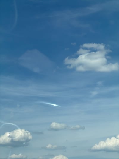 The image displays a clear blue sky with scattered white clouds. There are some light flares or reflections on the left side of the image, suggesting the photo was taken through a window or with a reflective surface. The clouds vary in size and density, with some appearing fluffy and well-defined, while others are more wispy and spread out. The overall impression is of a bright, possibly sunny day. The location, Тэльмінскі сельскі Савет, Belarus, indicates a rural or semi-rural setting. There are no people, specific objects, or discernible actions taking place in the image.