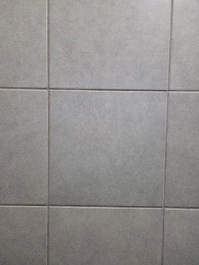 The image displays a head-on view of a uniform tiled surface, presenting a grid of square, light grey tiles with darker grey grout lines. The tiles possess a matte finish with a subtle, fine granular texture. The arrangement includes three full horizontal rows and extends across at least four vertical columns, with portions of tiles visible along the edges. No individuals, distinct objects other than the tiles, or ongoing actions are depicted. Identifiable environmental context or specific geographical markers, including a location within the city of Gevgelija, North Macedonia, are absent from the visual information provided.