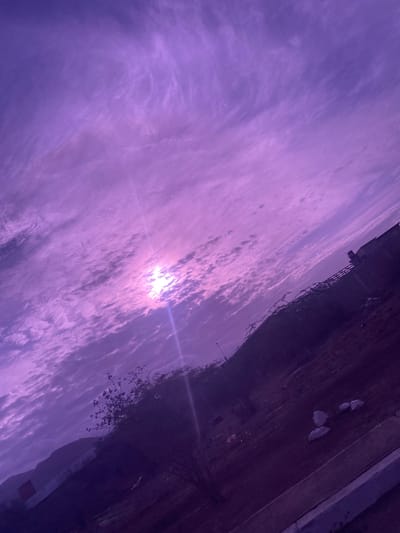 The image shows a sky with clouds, possibly taken in El Dátil, Venezuela. The sky is the dominant feature, with a bright light source (likely the sun) partially obscured by the clouds. A dark, undefined area is present at the top edge of the image, possibly depicting buildings or land. The image is rotated, giving an unusual perspective.