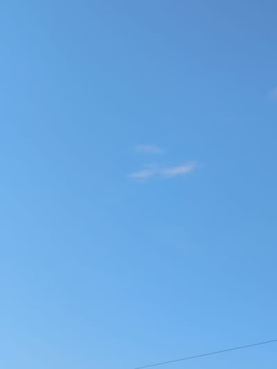 A clear, bright blue sky dominates the frame, with a few wispy clouds scattered sparsely. In the lower right portion of the image, a thin black wire is visible, stretching horizontally across the frame. The scene appears to be an outdoor shot, likely taken during the daytime, with no discernible city structures or landmarks visible to indicate a specific location within Abay, Kazakhstan. The focus is entirely on the sky and the faint presence of the wire.