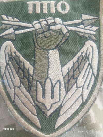 The image shows an embroidered patch with a military emblem. The emblem features a clenched fist holding arrows, with wings spread on either side. Below the fist is a trident symbol. The text "MTO" is embroidered in white capital letters across the top of the patch. The patch is affixed to a green fabric, likely a uniform. In the bottom left corner, the text "moto g06" is visible. In the bottom right corner, the date "6 лип. 2026 р." and time "19:36" are superimposed, indicating that this is likely a timestamp from a mobile device, suggesting the image was taken in Podvirky, Ukraine, on July 6, 2026, at 19:36. The environment appears to be outdoors, with the camouflage pattern of the uniform suggesting a military context.