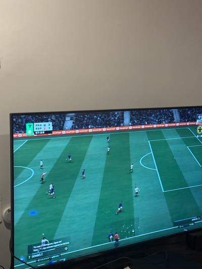 The image shows a television screen displaying a soccer video game. The game features a match between "FRA" (France) and "ESP" (Spain), with France leading 2-1 at 97:28 into the game. Player names like "DEMBÉLÉ" and "GARCÍA" are visible. The game is being played on a virtual stadium with spectators in the background. The environment appears to be a living room or entertainment space, with a wall visible in the upper portion of the image. There is no information to suggest the location is Mérida, Mexico.