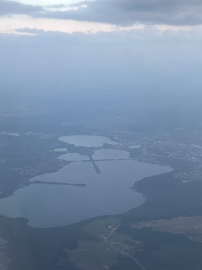 The image shows an aerial view of a lake complex near the city of Бордуки, Russia. The lakes are interconnected by narrow channels and surrounded by dense forests and urban development. The sky is overcast, suggesting a cloudy or hazy day.