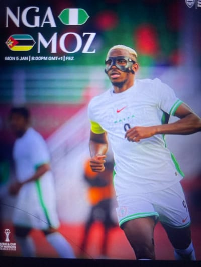 A promotional image displays a soccer player wearing a protective mask, likely Victor Osimhen. He is in a white jersey with green accents, seemingly for the Nigerian national team. The opposing team is Mozambique, represented by the abbreviation "MOZ" alongside the Mozambican flag. The graphic states "NGA" for Nigeria, accompanied by its flag. The game is scheduled for Monday, January 5th at 8:00 PM GMT+1 in FEZ. A small logo reading "AFRICA CUP OF NATIONS QUALIFIERS 2023" appears.