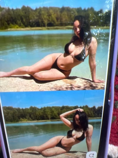 Two images are stacked vertically. The top image depicts a woman in a black bikini posing on a log by a body of water. She is lying on her side with one leg extended and the other bent. The background shows a lush green forest and a clear blue sky. The bottom image is a close-up of the same woman in a similar pose, this time with her hand resting on her head. She is also wearing a black bikini and is positioned on a log. The background again features a forest and a body of water. There is no indication of the city of Kara-Dıykan, Kyrgyzstan in this image.