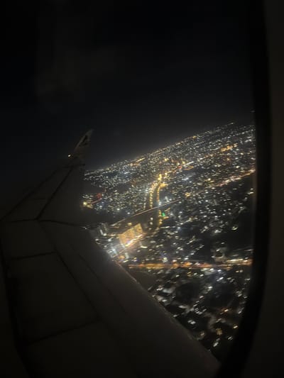 The image presents an aerial view of a sprawling city at night, seen from an airplane window. Countless artificial lights, primarily white and yellow, illuminate the urban landscape, appearing as a dense, shimmering carpet stretching across the right and central parts of the frame. The city lights suggest a significant metropolitan area.

A substantial portion of an airplane wing is visible in the lower right quadrant and extending towards the bottom of the image, showcasing its structural elements against the backdrop of the illuminated city. The dark frame of the airplane window is perceptible along the top and left edges, framing the nocturnal vista. The time of day is clearly night, with the sky appearing dark and free of clouds, allowing for a clear view of the city below. The scene captures the experience of flying over a city after dark, possibly during takeoff or landing due to the distinct detail of the ground. Based on the provided context, the location is Addis Ababa, Ethiopia. No people are visible, and there is no discernible text within the image.