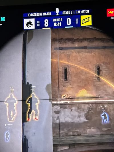 The image is a screenshot from a video game, likely Counter-Strike: Global Offensive, displaying the user interface and in-game elements. At the top is a scoreboard indicating "IEM COLOGNE MAJOR STAGE 3 | 0-0 MATCH". One team's score is 8, and the other's is 0. The round is number 9, with 0:41 remaining. The logo for the team "Natus Vincere" (NAVI) is visible.

In the foreground, several player silhouettes are highlighted with glowing auras, indicating their presence and status in the game. Some silhouettes have player names displayed above them, such as "donk", "mjgixx", "TA BOZZER", and "bilt". Weapons icons are also visible above some names. One player silhouette is distinguished by red shoes.

The environment appears to be an urban setting with textured walls, suggesting an in-game map. There are two small, dark rectangular openings in the wall. A bright orange projectile trail streaks across the background. The overall image quality is pixelated, consistent with a video capture. There is no information in the image to suggest the location is Gothenburg, Sweden.