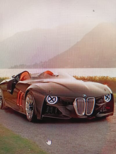 A dark-colored concept car, possibly a BMW, is parked on a paved surface with some grass to the left. The car is a convertible with orange accents visible in the cockpit. The front of the car features a distinctive grille and headlights. In the background, a body of water is visible, with mountains or hills beyond. The sky is overcast and appears to be at either sunrise or sunset. There are no people or any discernible signs of the city of Sluck, Belarus in the image.