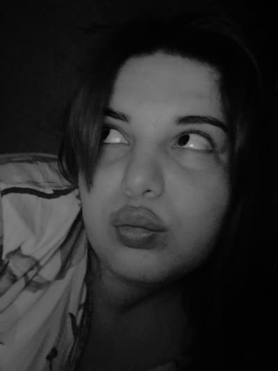 A close-up, black-and-white photograph shows a person's face, possibly female, tilted at an angle. The subject is looking upwards with both eyes. Their lips are slightly puckered. A patterned fabric, possibly clothing or bedding, is visible in the background behind their head. The rest of the background is dark and indistinct. There is no evidence of a location in the city of Амзя, Russia.