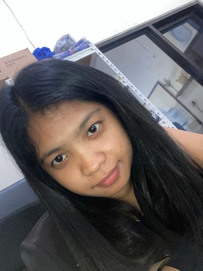 The image is a close-up selfie of a person with dark hair. The person is indoors, presumably in a room with a window and various items, including a box labelled "Wonderful Gift". The location cannot be determined to be in the city of Negara, Indonesia.