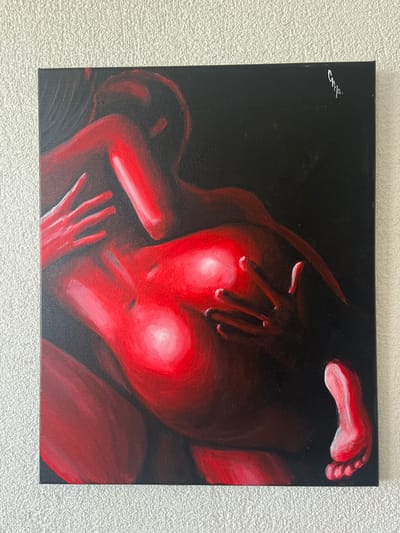 This is a painting of two intertwined human forms rendered in shades of red and black. The subjects are positioned in a way that suggests an intimate or sensual embrace. One figure's hand is placed over the other's face, obscuring it. The overall tone of the painting is dramatic, with strong contrasts between the luminous red and the dark background, creating a sense of depth and intensity. There is a signature on the top left corner of the painting, which appears to be "Samp" in silver lettering. The painting is displayed against a textured white wall. The location context provided (Balaklavsky district, Ukraine) is not visually discernible from the image itself.