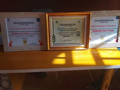The image shows three framed certificates of achievement from "SALAHMARDOOH FHG ORG. LIMITED" arranged on a wooden table. The certificate on the left and right highlight achievement for "Top 10 Highest Personal Point in a Year" and "Top 10 Personal Sponsoring" respectively, both awarded to Godwin Matthew for performance in the 2023 business year. The central certificate is also awarded to Godwin Matthew & Oshi (9) for the 2024 business year, but in the category of “Top 10 Personal Sponsoring” with a first-place ranking. The specific location (Oke Ogun, Nigeria) is not identifiable in the image.