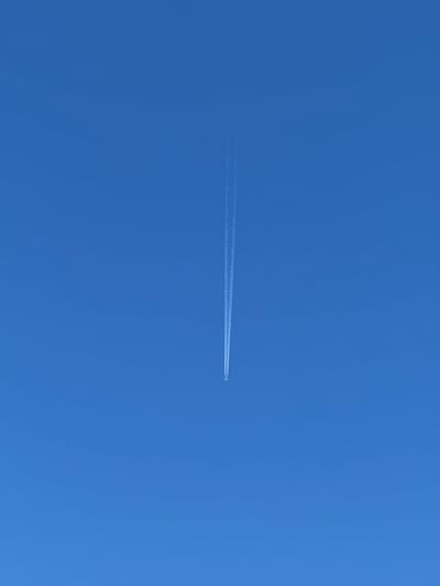 An airplane leaves a white contrail as it flies across a clear, bright blue sky. The airplane is small and appears at the bottom center of the image. The contrail stretches upwards from the plane, tapering off as it ascends. The image is devoid of any landscape or city elements, focusing solely on the aircraft's passage through the atmosphere. It is not possible to determine the location in the city of Slavyani, Bulgaria from this image.