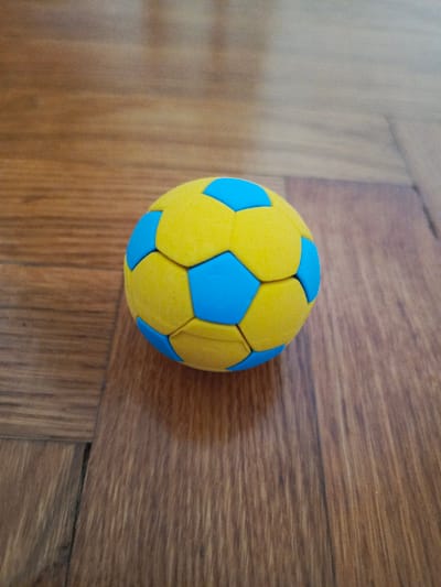 A yellow and blue soccer ball rests on a wooden floor. The ball is textured and has a pattern of pentagons and hexagons. The floor appears to be made of wood planks with a visible grain. The lighting suggests an indoor setting. There are no people or actions depicted. The location in Biaroza, Belarus, is not discernible from the image.