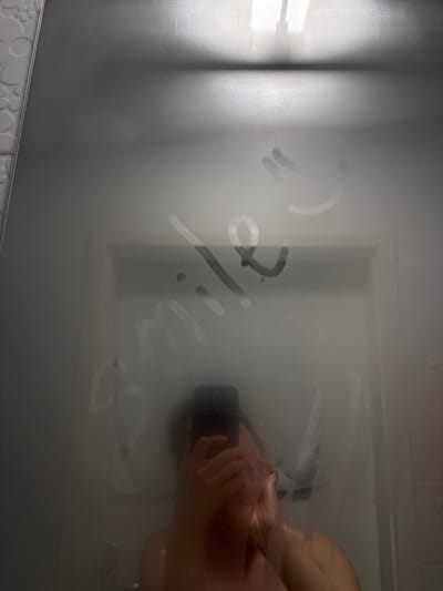 The image shows a steamy bathroom mirror in Kranj, Slovenia. Written on the fogged glass is the word "Sorry." Reflected in the mirror is an obscured figure inside a shower or bath area, seemingly washing their hands.