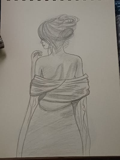 The image displays a graphite pencil sketch on a light-colored, spiral-bound sheet of paper, likely from a sketchpad. The drawing features a female figure depicted from the back, with her head turned to her left, showing a partial profile. Her hair is styled in a voluminous, intricate updo with multiple discernible strands and coils. Her upper back and shoulders are visible, suggesting a bare-shouldered appearance, with a draped garment or fabric loosely wrapped around her arms and falling alongside her body. The fabric is rendered with shading to indicate folds and texture. The subject's left hand is raised to the area near her neck, with fingers gently curled. The drawing employs varied pencil strokes and shading for depth. The sketchpad's spiral binding is visible along the top edge of the paper. The paper rests on a surface, with a dark, possibly wooden, edge visible at the bottom of the frame and a blue and white patterned textile visible along the right side. A small, dark, indistinct object is partially visible on the left edge of the sketchpad. This image was captured in 서대문구, South Korea.