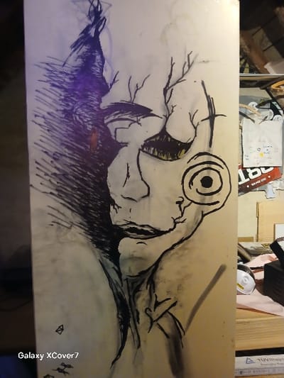 A charcoal drawing dominates the image. A stylized figure with a circular eye lies horizontally. Sparse branches sprout above its head, contrasting with dense, dark hatching that forms a textured base below. Soft shading suggests a landscape, while stark lines define the figure. The composition employs stark contrast and textural variation, resulting in a visually dynamic scene.