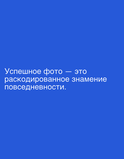The image is a vertical, medium shot of a solid blue background with white text. The text reads "Успешное фото — это раскодированное знамение повседневности." This translates to "A successful photo is a decoded sign of everyday life." The text is centered horizontally and positioned towards the bottom of the frame. There are no people, objects, or environmental details other than the text and the blue background. The location of Even Yehuda, Israel is not depicted or implied in the image.
