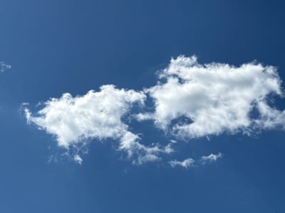 The image captures a clear, expansive blue sky above Kochetok, Ukraine, on what appears to be a bright day. Dominating the central horizontal plane is a prominent, elongated cloud formation. This cloud is primarily white and fluffy, with characteristics of cumulus clouds, displaying varying densities from wispy, translucent edges to more opaque, brighter sections. The sunlight illuminates the cloud, highlighting its texture and irregular shapes.
The sky is a consistent, deep blue, indicating a lack of widespread cloud cover, suggesting fair weather. To the far left, a few smaller, less defined wisps of cloud are faintly visible. The main cloud stretches horizontally across the frame, with its left side appearing somewhat more dispersed and its right side more consolidated and voluminous. There are no people, man-made objects, or discernible text within the image. The scene conveys a sense of calm and natural vastness, typical of a clear sky with scattered clouds during daylight hours.