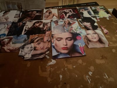 The image displays a collection of magazine cutouts scattered across a brown, textured surface, likely a table or floor. The cutouts feature various models and advertisements, predominantly focusing on fashion, beauty, and personal care products. Several close-ups of female faces with makeup are visible, along with images of couples and individuals in stylized poses. Some of the cutouts include text in Russian, such as "THE ONE," "MSI," and brand names related to cosmetics and fragrances like "ORIFLAME." There are also scattered pieces of white paper or tape, suggesting the cutouts are not neatly arranged. The background of the image is blurred, but hints of wooden structures and possibly other printed materials are present. The overall impression is one of a creative or organizational project, perhaps a mood board or collage. There is no indication of the specific location within Bulgunnyakhtakh, Russia.