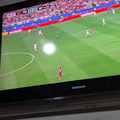 The image shows a television screen displaying a soccer match. The score is tied at 0-0 between Portugal (POR) and Spain (ESP), with the game at 30:38. Players in red and white uniforms are visible on the green field. The Samsung logo is present on the bottom bezel of the TV. The background shows a crowd of spectators in stadium seating. The image itself is a photograph of the television screen. No specific location in the city of Peshtera, Bulgaria can be determined from this image.