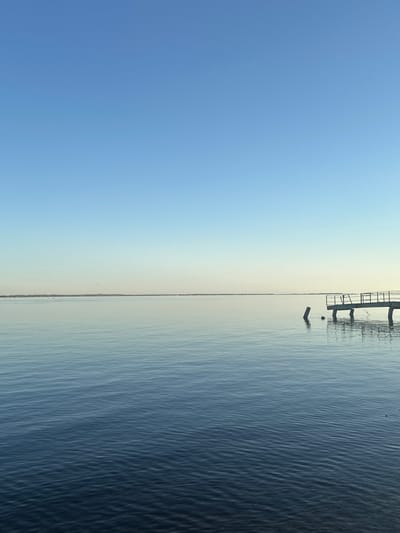 The image shows a body of water under a clear blue sky. A structure resembling a pier is visible on the right side, partially extending into the water. The water's surface shows subtle ripples. The location is likely near Soroch'i Gory, Russia, based on the likely origin of the image. There are no people visible in the scene.