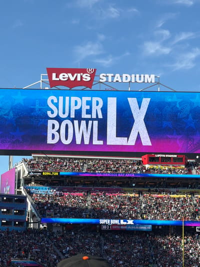 Levi's Stadium displays "SUPER BOWL LX" in large letters alongside the Levi's logo. Below, a smaller sign shows "$291,725", and "SAN FRANCISCO BAY AREA". A narrow vertical sign shows "SUPER BOWL LX" and "38:31 SEATTLE SEAHAWKS". The stadium is densely packed with spectators.