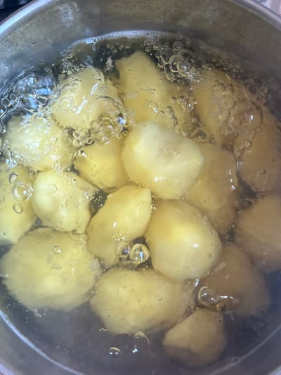 The image shows small, whole, boiled potatoes in a pot of water. The water is bubbling, indicating that it is hot. Some of the potatoes are partially submerged in the water, while others are fully covered. The potatoes are a light yellow color and appear to be soft. The pot is made of stainless steel and has a thick rim. The scene appears to be in a kitchen.
There is no information in the image to suggest this is in Kramatorsk, Ukraine.