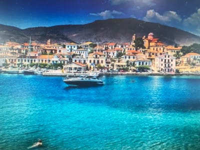 This media file depicts a vibrant coastal town with a mountain backdrop, set against a clear blue sky and shimmering turquoise water. The town features a dense collection of buildings with terracotta roofs and white or ochre-colored walls, characteristic of Mediterranean architecture. A prominent domed church, painted in warm orange hues, stands out amongst the buildings, hinting at a rich history and culture.
In the foreground, the crystal-clear water allows a view of the seabed in some areas, while its surface is gently rippled. A modern motor yacht is moored in the bay, its sleek design contrasting with the traditional architecture of the town. Further out in the water, a person can be seen swimming, enjoying the refreshing sea. The scene suggests a warm, sunny day, likely in the late morning or early afternoon, given the bright sunlight casting reflections on the water.
The overall atmosphere is one of tranquility and leisure, with the stunning natural beauty of the coastline blending seamlessly with the charming urban landscape. The image evokes a sense of a peaceful holiday destination, inviting viewers to imagine themselves enjoying the sun, sea, and local culture. No visible text is present in the media file.