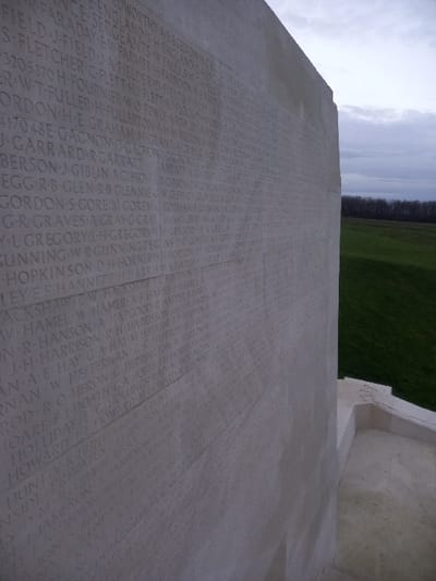 The image shows a stone memorial engraved with names. The names are arranged in columns, likely alphabetical, and include surnames like "ORTHY," "FARADAY," "FLETCHER," and "FOURNIER." Other names include "GARRARD," "GIBLIN," "GLEN," "GRAVES," and "GUNNING." Some entries appear to have initials or rank before the surname. The names are etched into the stone's surface, and the memorial is positioned against a backdrop of sky, greenery and a structure.