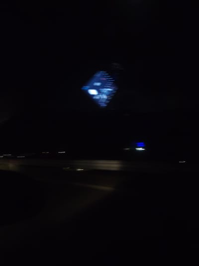 The image appears to be taken from inside a vehicle at night. The blurry lights of a car's dashboard are visible in the top center of the image. Outside, there's a blurry view of a road, along with the lights of other vehicles and buildings. It is not possible to ascertain the location in the city of Jeleznitsa, Bulgaria.