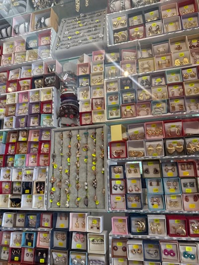 This image depicts a large display of jewelry, likely for sale. The jewelry consists of rings, earrings, necklaces and bracelets organized in small boxes, arranged closely together, covering a significant area, likely a store shelf or display case. The jewelry varies in style and color, including gold, silver, and colored stones. Prices are indicated on the jewelry and packaging. The location of this image is the city of San Cristóbal, Mexico.