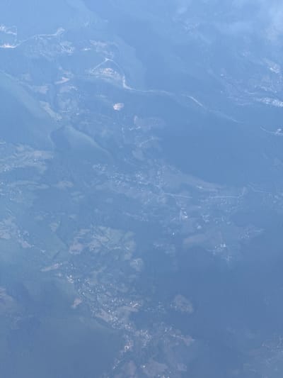 This is an aerial photograph showing a rural landscape with scattered settlements. The terrain is mountainous and covered with dense vegetation, likely forests and agricultural fields. Several small villages or hamlets are visible, characterized by clusters of buildings and connected by winding roads. A river or stream appears to be a prominent feature, carving its way through the landscape. The overall impression is one of a remote, undeveloped area.
Specifically, the image depicts the area of Tihovići, Bosnia and Herzegovina. The presence of the villages, the rugged terrain, and the vegetation are consistent with the geographical characteristics of this region. No individuals or specific actions are discernible from this aerial perspective. The focus is on the landscape and human settlements within it.