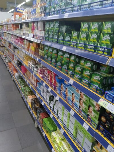 A supermarket aisle displays shelves stocked with various soaps. Irish Spring soaps are stacked high on the top shelves. Below, a variety of other soap brands are arranged, including "Ivory". Price tags are visible, such as one reading "TE 410.00". The shelves are blue and yellow, and the floor is gray. The perspective suggests the image was taken at the end of the aisle.