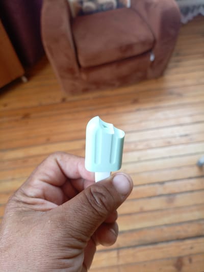 The image shows a close-up of a person's hand holding a light blue plastic object, possibly a cap or applicator. The object is positioned in the foreground. In the background, a brown armchair is visible, and a wooden floor occupies the lower portion of the image. The overall lighting suggests an indoor setting. The location of Churapcha, Russia, is not depicted in this image.