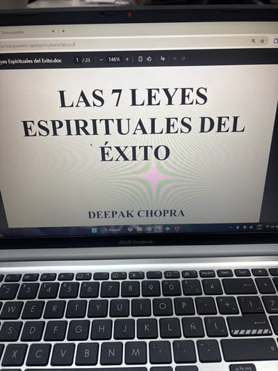 The image captures a close-up, top-down view of an open laptop, tilted on its side, showing both its screen and a portion of its keyboard. The laptop's screen displays a document, likely a PDF, open in a web browser or a document viewer.

The main content on the screen is a title page for a book. The title, prominently displayed in large, dark serif font, reads: "LAS 7 LEYES ESPIRITUALES DEL ÉXITO," which translates from Spanish to "The 7 Spiritual Laws of Success." Below the title, also in dark serif font, is the author's name: "DEEPAK CHOPRA." The background of the document is a light cream or white color, with subtle, faint horizontal lines or striations visible across the surface, possibly an artifact of the screen's refresh rate or the camera capture.

Along the top edge of the screen, the interface of the document viewer or web browser is visible. On the far left, "Nueva pestaña" (New tab) is displayed, next to a file path that reads "mentos/goe/sieteleyesEspiritualesdel Exito.pdf" and "yes Espirituales del Exito.doc," suggesting the file is a PDF version of a document with a similar name. Below this, there are navigation and zoom controls, showing "1/23" indicating page 1 of 23, and a zoom level of "146%." Other icons for downloading, printing, and sharing are also present. In the top right corner of the screen, system information such as the time "09:41 AM", a Wi-Fi symbol, and a battery icon are visible, along with "ESP LAA" likely indicating the language settings. At the very bottom of the screen, a taskbar or dock shows a search icon labeled "Q Búsqueda" (Search), followed by a browser icon and other application icons, and the laptop's brand name "ASUS Vivobook."

To the right of the laptop screen, the silver-colored keyboard is partially visible. The keys are black with white lettering, typical of a laptop keyboard. The layout appears to be Spanish, evidenced by keys like "Ñ" and various accented vowels and symbols (e.g., "¿", "¡"). Function keys F1 through F12 are visible at the top, along with media controls and special function keys like "Imp pant" (Print Screen), "Insert," "Supr" (Delete), "Inicio" (Home), and "Re pag" (Page Down). The numeric row from 7 to 0 and symbols like "*", "+", "-", are also clearly visible. The spacebar is partially obscured at the bottom.