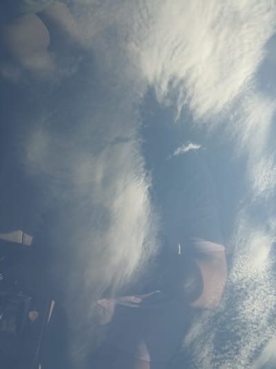 The image appears to be taken from inside a vehicle looking out at a sky filled with wispy white clouds against a blue sky. The perspective suggests the camera is angled upwards, possibly reflecting off the car's windshield. In the lower portion of the image, the interior of the vehicle is visible, including parts of the dashboard, a windshield wiper, and possibly a seat. There are no people clearly visible in the image. The overall impression is of a cloudy day, seen from the interior of a car. The location in Tairove, Ukraine is not discernible from the visual information in the image.