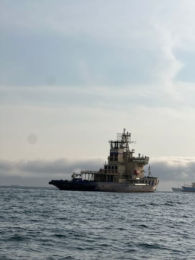 The image shows a large vessel at sea, likely a specialized ship for offshore operations. The vessel is light-colored with complex superstructure including antennas, cranes, and multiple decks. The ship's name "POCMOPEOPTA" is visible on the hull. The sea is choppy and the sky is overcast. The location cannot be determined from this image alone, as it only shows the vessel at sea. Novomoskovsk is a city in Russia with no direct access to the sea, thus this photo would not be taken in Novomoskovsk.