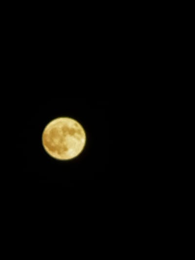 The image shows a full moon against a black sky. The moon is a yellowish-orange color and appears to have some texture visible on its surface. It is positioned in the left half of the frame. The rest of the image is completely black, indicating a night scene with no other visible light sources or objects. There are no people, buildings, or any other environmental features visible. Therefore, it is not possible to determine any specific location within the city of Santiago De Compostela, Spain, or any actions or interactions.