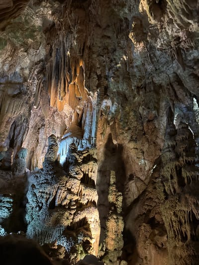 The image depicts the interior of Resava Cave, located in the Despotovac Municipality, Serbia. The scene showcases various cave formations, including stalactites and stalagmites. The rock formations appear layered and textured. Lighting within the cave highlights the intricate details of the stone surfaces. No people or other discernible subjects are present.