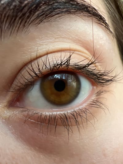 A close-up, eye-level shot focuses on a human eye with brown irises and dark lashes. The eye is open, with the pupil clearly visible and reflecting light. The skin around the eye shows pores and subtle texture. The image does not contain any information about the city of Ust-Chorna, Ukraine, or any environmental context.