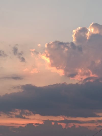 The image depicts a cloudy sky with warm hues of orange and pink, suggesting either a sunrise or sunset. The clouds are a mix of dark, ominous formations and lighter, illuminated ones, with sunlight breaking through in places, creating a dramatic effect. The scene appears to be an outdoor shot, likely taken from a vantage point within the city of Lozova, Ukraine, given the context provided. There are no visible people, subjects, or specific objects that indicate a particular location within the city, other than the implied presence of urban structures implied by the overall framing of the sky. The environment is solely characterized by the atmospheric conditions and cloud formations.