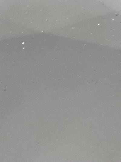 The image shows a close-up of a light gray, textured surface with several small, bright, irregularly shaped specks scattered across it. These specks appear to be reflective, suggesting they could be glitter, dust, or small particles of a foreign substance. The background is uniformly gray and out of focus, with no discernible environmental details or recognizable landmarks that would indicate a specific location in Kovachite, Bulgaria. There are no people, objects, or actions depicted in the image. The lighting is soft and diffused, casting no harsh shadows.