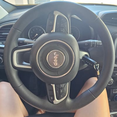 The image shows a close-up view of the steering wheel and dashboard of a Jeep vehicle. A key is inserted into the ignition. The steering wheel has various buttons, including controls for audio and cruise control. The Jeep logo is visible in the center of the steering wheel. The dashboard includes the instrument cluster with gauges. The image is taken from the perspective of someone sitting in the driver's seat. The location is identified as Cuarte de Huerva, Spain.